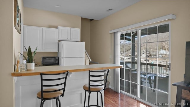 kitchen featuring visible vents, a breakfast bar area, a peninsula, freestanding refrigerator, and white cabinets