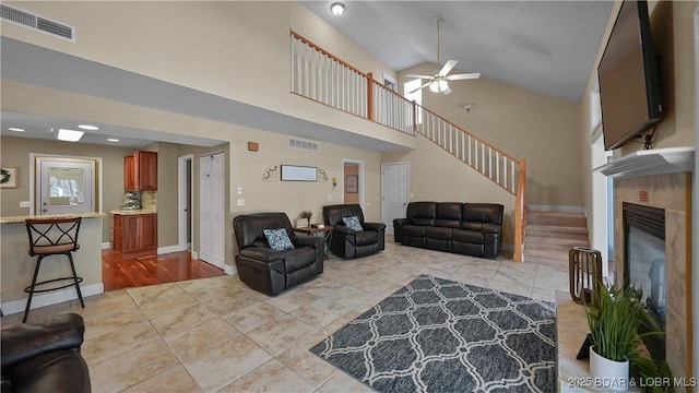 living area featuring a tiled fireplace, visible vents, high vaulted ceiling, and a ceiling fan