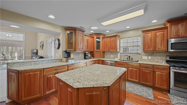 kitchen featuring light stone counters, a sink, stainless steel appliances, glass insert cabinets, and a center island