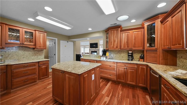 kitchen with glass insert cabinets, light stone countertops, dishwasher, and dark wood-style floors