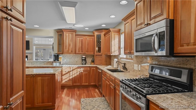 kitchen with a sink, stainless steel appliances, glass insert cabinets, and brown cabinetry