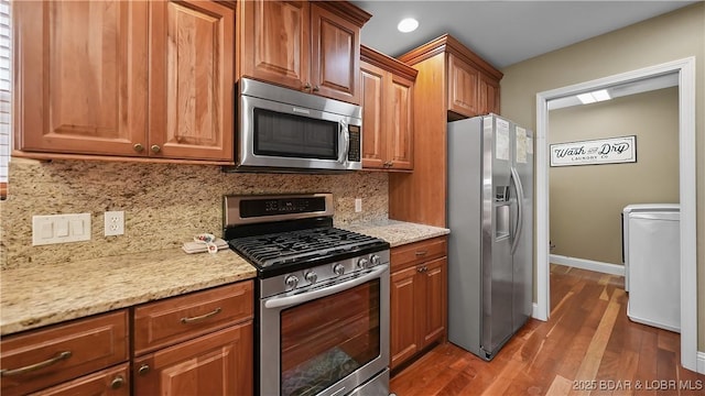 kitchen with dark wood-type flooring, light stone countertops, decorative backsplash, appliances with stainless steel finishes, and washer / clothes dryer