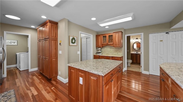 kitchen featuring light stone counters, decorative backsplash, dark wood-type flooring, washing machine and dryer, and brown cabinets