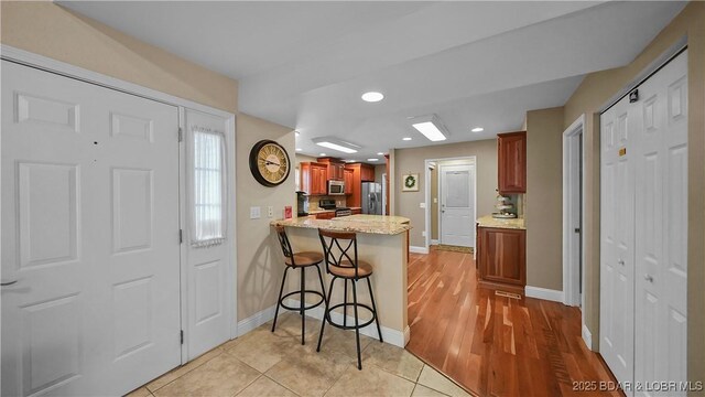 kitchen with baseboards, recessed lighting, a kitchen breakfast bar, appliances with stainless steel finishes, and a peninsula