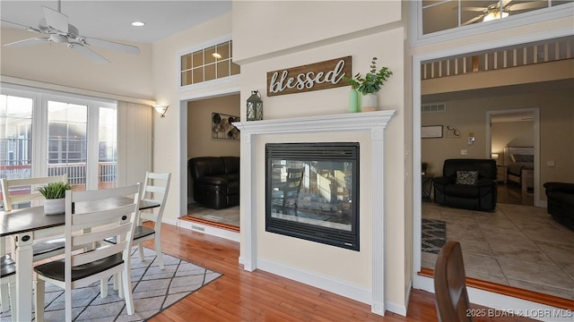 dining space featuring visible vents, a ceiling fan, wood finished floors, baseboards, and a multi sided fireplace