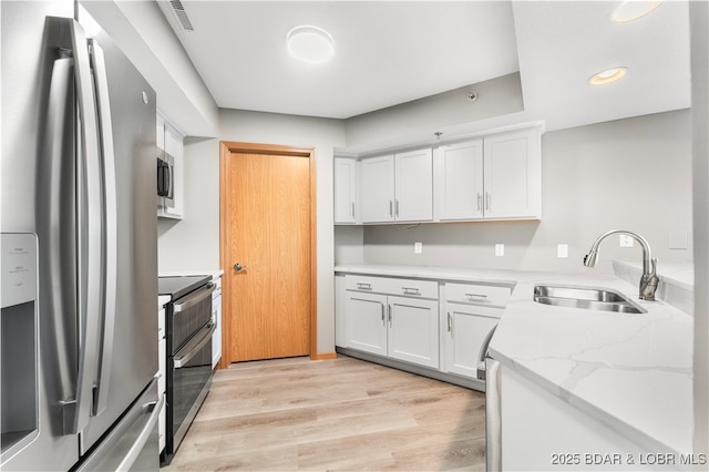 kitchen featuring visible vents, light wood-style flooring, a sink, stainless steel appliances, and white cabinets