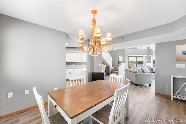 dining space with baseboards, a notable chandelier, light wood-style flooring, and stairs