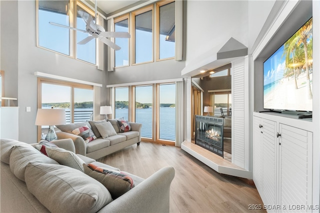 living area featuring a glass covered fireplace, wood finished floors, and ceiling fan