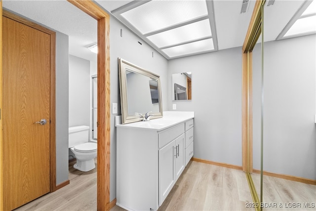 bathroom featuring visible vents, toilet, wood finished floors, baseboards, and vanity