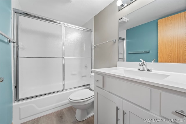 bathroom with vanity, toilet, wood finished floors, and enclosed tub / shower combo