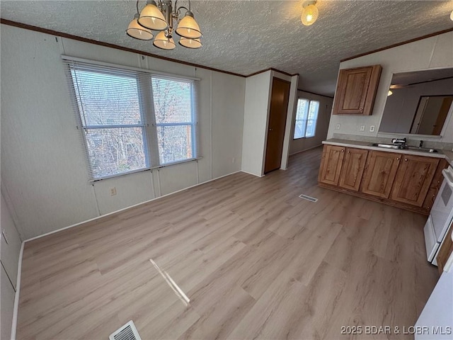 kitchen with brown cabinetry, light countertops, light wood-style floors, crown molding, and a notable chandelier