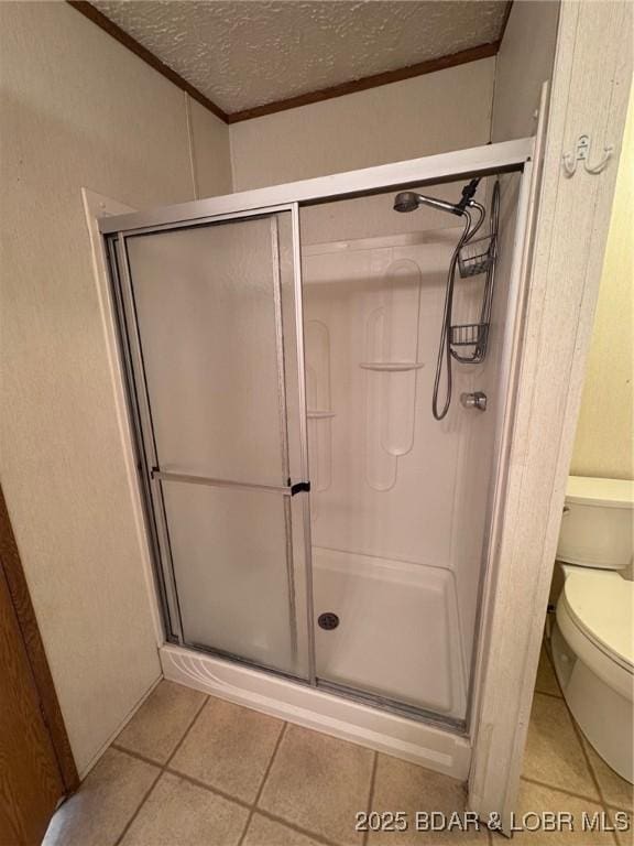 bathroom featuring a shower stall, toilet, tile patterned floors, and a textured ceiling