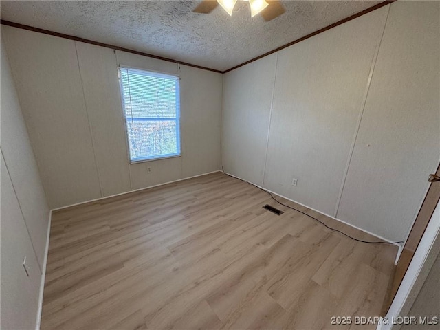 unfurnished room featuring wood finished floors, visible vents, ceiling fan, a textured ceiling, and crown molding