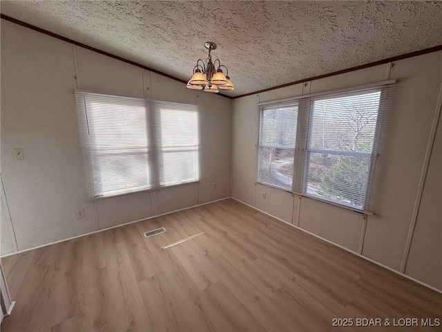 unfurnished dining area with visible vents, a textured ceiling, an inviting chandelier, crown molding, and light wood finished floors