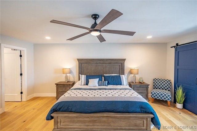 bedroom with light wood finished floors, recessed lighting, baseboards, and a barn door