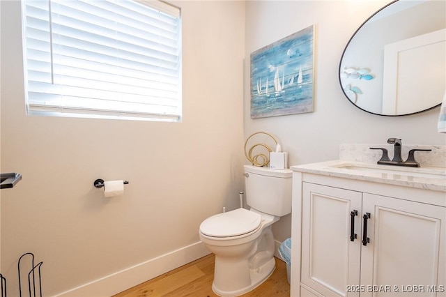 bathroom with vanity, toilet, wood finished floors, and baseboards