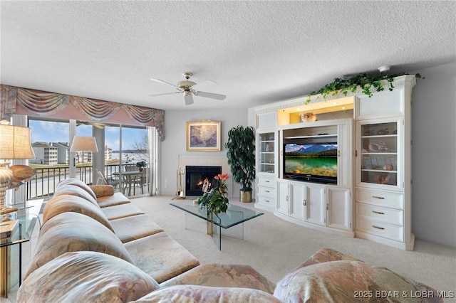 carpeted living area with a textured ceiling, a warm lit fireplace, and a ceiling fan