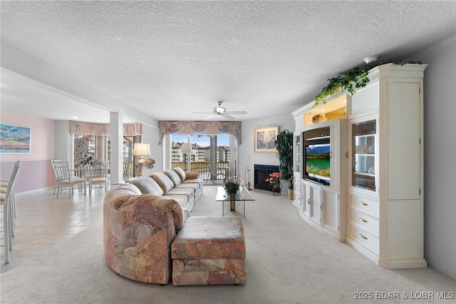 living room with light carpet, a warm lit fireplace, a textured ceiling, and ceiling fan