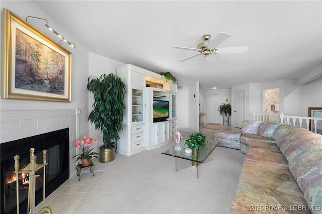 living room featuring light colored carpet, ceiling fan, a tiled fireplace, and a textured ceiling