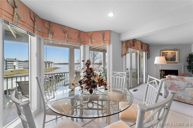 dining space featuring light tile patterned floors, visible vents, a textured ceiling, and a warm lit fireplace