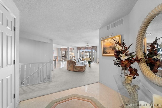 corridor with visible vents, carpet, an upstairs landing, tile patterned floors, and a textured ceiling