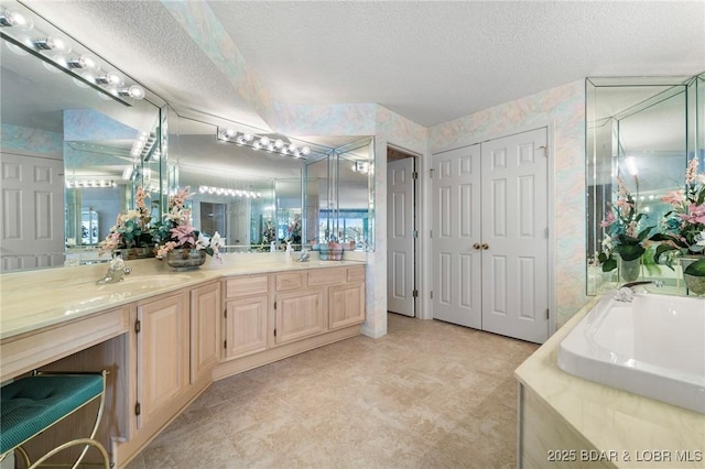 bathroom featuring a textured ceiling, vanity, and wallpapered walls