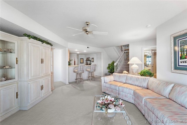 living area with bar, stairway, light carpet, and ceiling fan