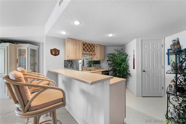 kitchen with visible vents, light brown cabinets, a textured ceiling, backsplash, and light countertops