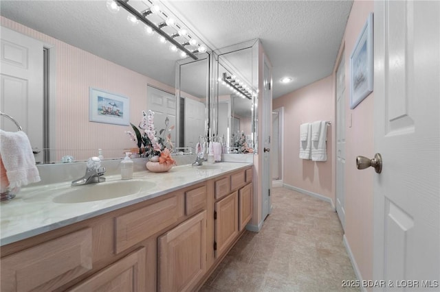 bathroom with a stall shower, a sink, a textured ceiling, double vanity, and baseboards