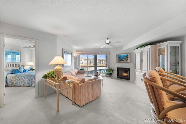 living area featuring a fireplace with flush hearth, light colored carpet, a ceiling fan, and a textured ceiling