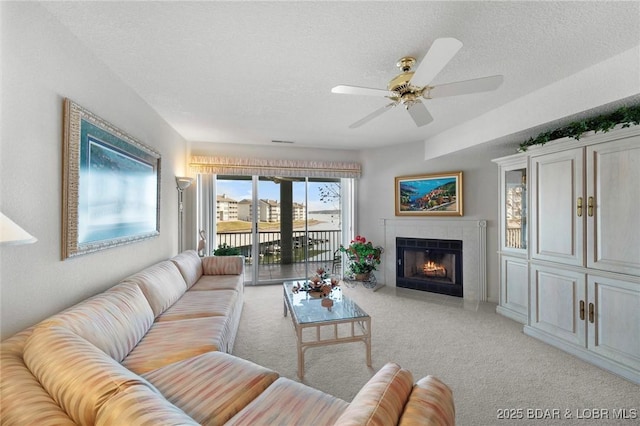 living room featuring light carpet, a fireplace, a textured ceiling, and a ceiling fan