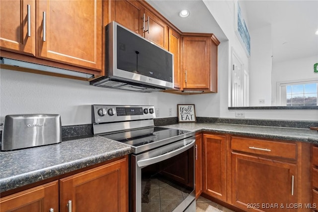 kitchen with light tile patterned floors, brown cabinetry, recessed lighting, stainless steel appliances, and dark countertops