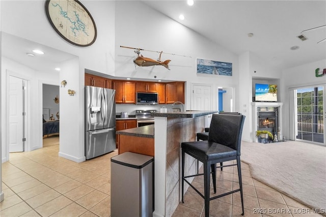 68 Lighthouse Rd Unit 344, Lake Ozark, MO 65049 - kitchen featuring appliances with stainless steel finishes, high vaulted ceiling, dark countertops, light tile patterned floors, and a kitchen breakfast bar