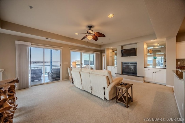 living area with a glass covered fireplace, a ceiling fan, baseboards, and light carpet