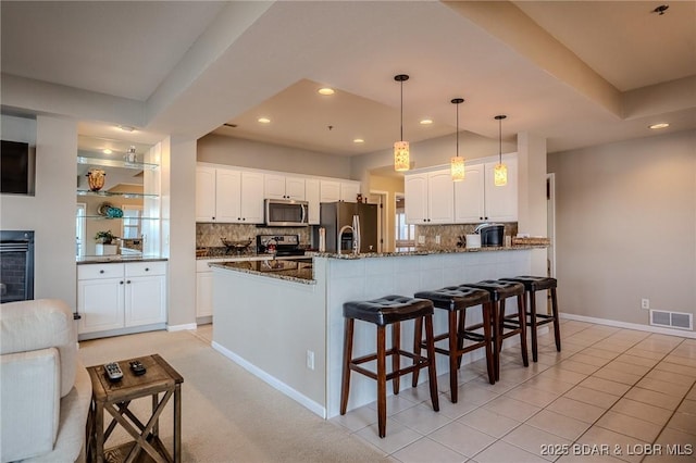 kitchen featuring visible vents, dark stone counters, a peninsula, stainless steel appliances, and white cabinetry