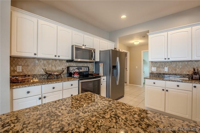 kitchen featuring dark stone countertops, backsplash, stainless steel appliances, white cabinets, and light tile patterned floors