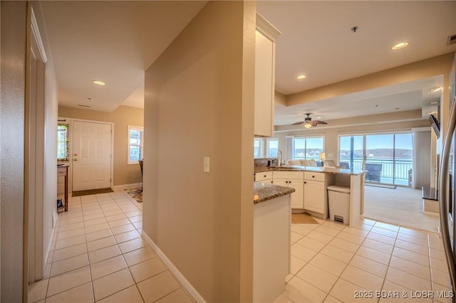 kitchen featuring light stone countertops, baseboards, a peninsula, light tile patterned flooring, and white cabinetry