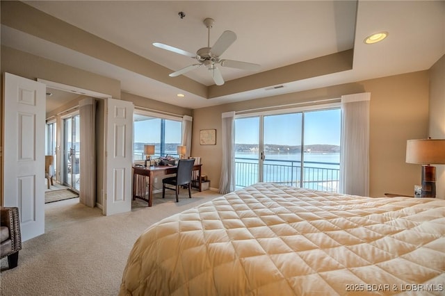 carpeted bedroom with visible vents, a water view, a tray ceiling, recessed lighting, and access to outside