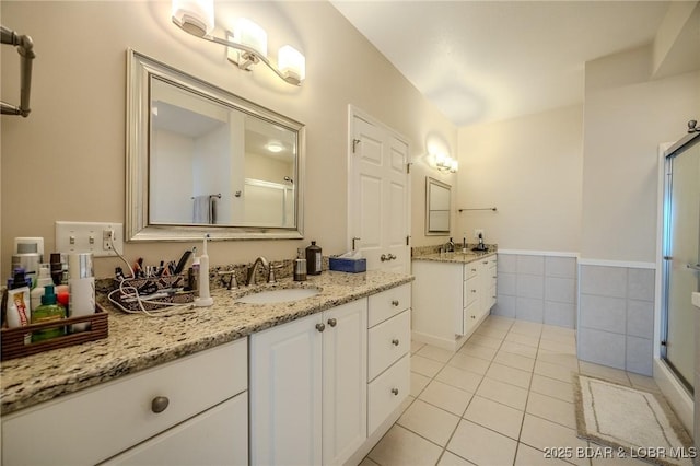 bathroom featuring two vanities, a stall shower, a sink, tile walls, and tile patterned flooring