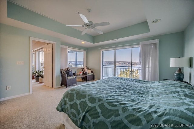 carpeted bedroom with a ceiling fan, baseboards, a tray ceiling, access to exterior, and a water view