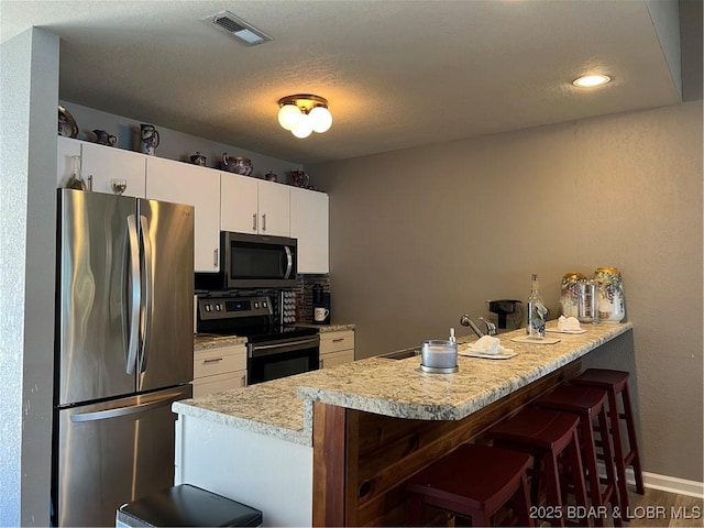 kitchen featuring visible vents, a kitchen bar, appliances with stainless steel finishes, a peninsula, and light countertops