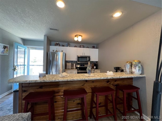 kitchen with white cabinetry, a kitchen breakfast bar, visible vents, and appliances with stainless steel finishes