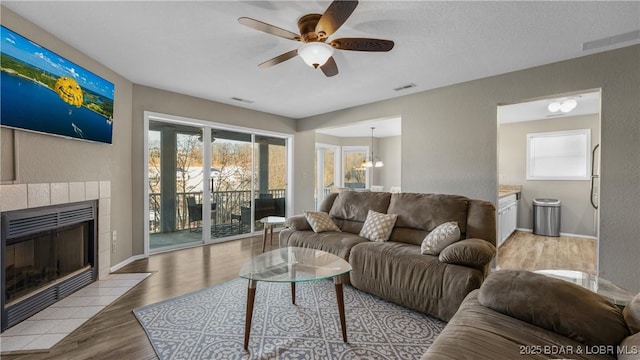 living area featuring visible vents, a tiled fireplace, wood finished floors, a textured wall, and a ceiling fan