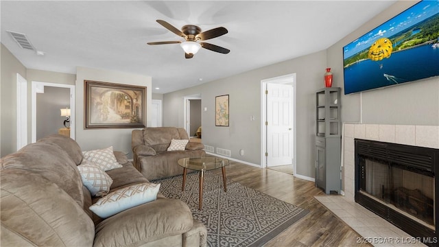 living room with visible vents, wood finished floors, a ceiling fan, and a tiled fireplace