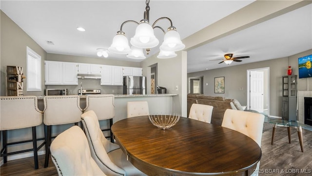 dining area featuring ceiling fan with notable chandelier, recessed lighting, dark wood-style floors, and a fireplace