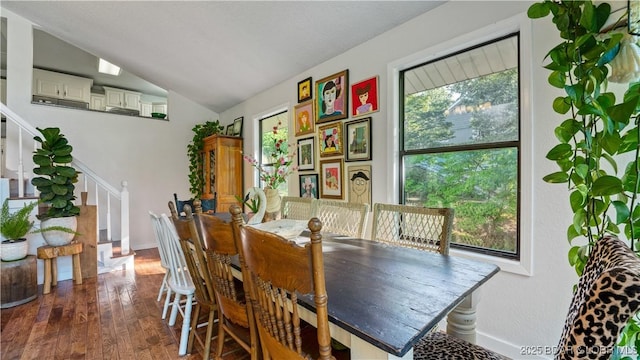 dining space featuring wood-type flooring, baseboards, vaulted ceiling, and stairway