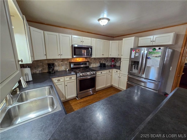 kitchen featuring decorative backsplash, dark countertops, white cabinetry, a sink, and stainless steel appliances