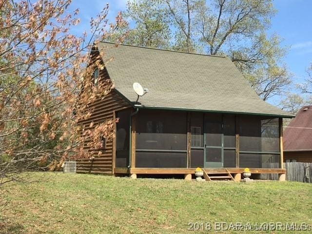 back of house with a sunroom, a yard, and roof with shingles