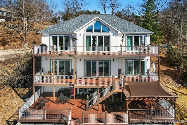 rear view of house with stucco siding, a balcony, roof with shingles, and french doors