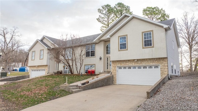 raised ranch featuring a garage, concrete driveway, and stone siding
